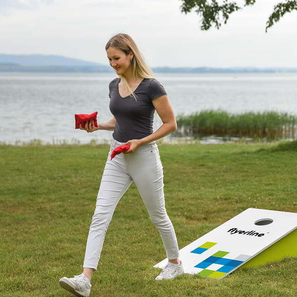 Frau mit roten Wurfsäckchen neben Cornhole-Brett am See